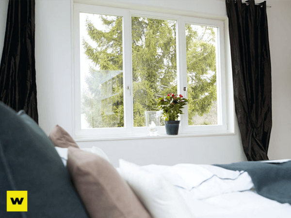 Helles Schlafzimmer mit großem Fenster, Blick ins Grüne und Zimmerpflanze auf Fensterbank.
