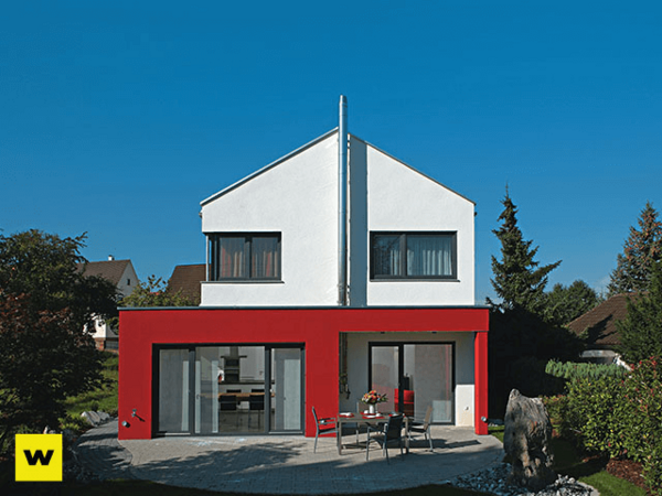 Modernes Einfamilienhaus mit Flachdach, roter Fassade und Garten bei blauem Himmel.