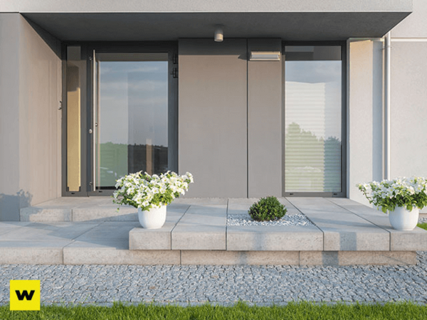 Moderner Hauseingang mit großen Glasflächen, Steinplatten und weißen Pflanzkübeln im Vorgarten.