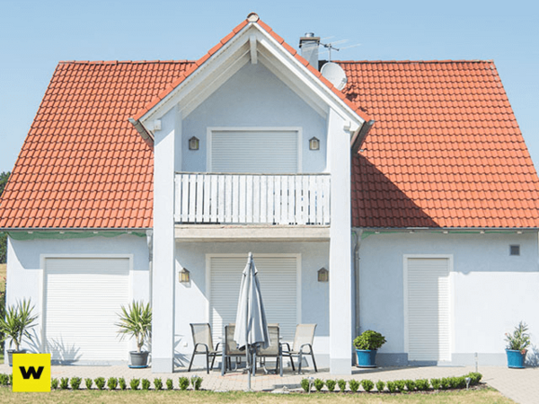 Modernes Einfamilienhaus mit rotem Dach, Terrasse und Garten bei sonnigem Wetter.
