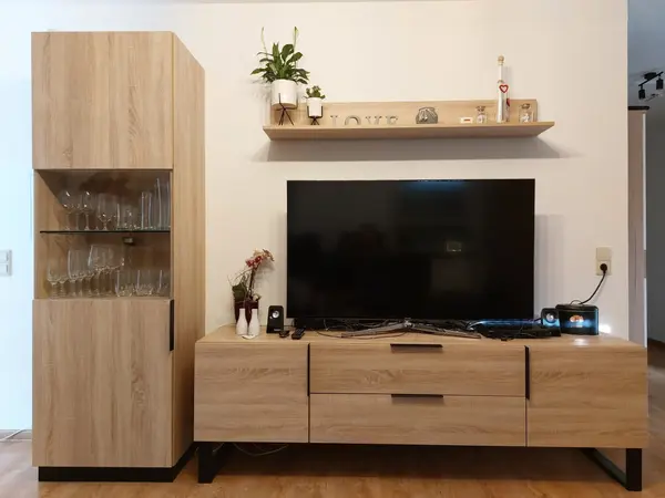 Wohnzimmer mit Holz-Wohnwand, Gläser-Vitrine, großem Fernseher und Dekoration.